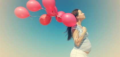 pregnant woman is enjoying the sun with balloons in hand